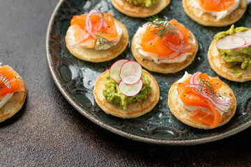 Mini blini pancakes with soft cheese, cold smoked salmon and guacamole