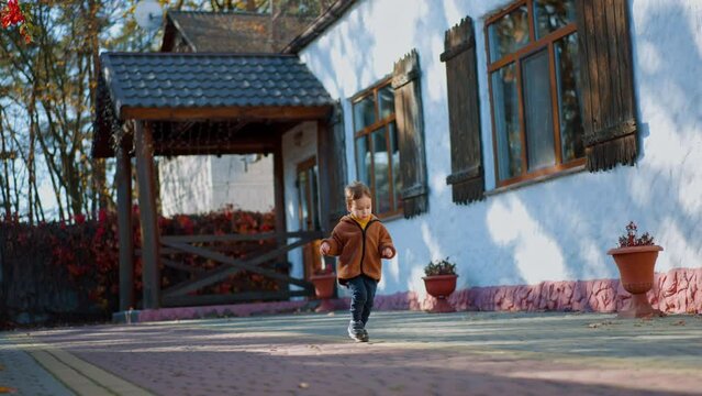 Caucasian toddler wearing brown jacket and blue pants runs outdoors. Good time outside in autumn.