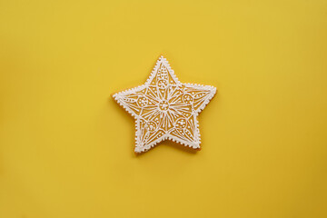 Glazed openwork white gingerbread star lies on a yellow background