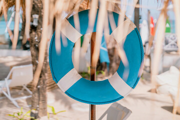 Blue white lifebuoy hang under tropical palm leaf umbrella, leafs are blurred. Close up photo