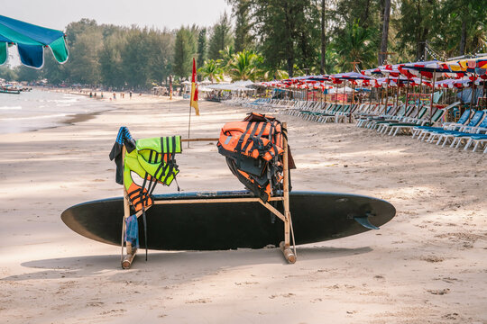 Wooden hanger with many safety life jackets with surfboard on an empty sandy beach close to shoreline, early morning, no tourists. Close up photo