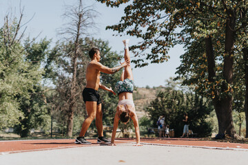 Two fit athletes practice and compete in sports outdoors on a sunny day. Enjoying the natural environment, they do handstands and exercise surrounded by plant life.