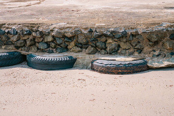 Old car tires used as for strengthening concrete sidewalk area built on sandy beach at high tide water level, front view - obrazy, fototapety, plakaty