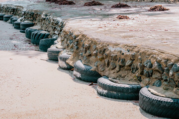 Old car tires used as for strengthening concrete sidewalk area built on sandy beach at high tide water level, perspective view - obrazy, fototapety, plakaty