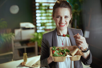 smiling business owner woman in green office eating salad