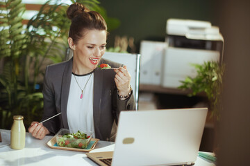 smiling woman employee in green office eating salad