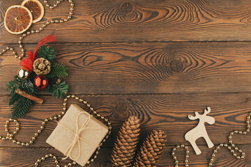 Christmas holiday background with wooden deer, tree decorated with pine cone, beads and gifts wrapped in craft paper, dried oranges on rustic wooden background, flat lay, copy space.