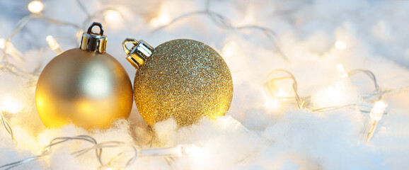 Two golden Christmas balls on a background of garland shining lights and snow. Christmas decor...