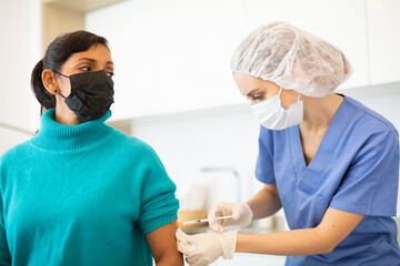 Young adult woman in medical face mask getting vaccinated at doctors office, coronavirus or flu vaccination - obrazy, fototapety, plakaty