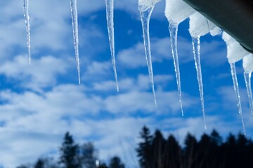 Closeup of ice dams hanging from a roof with cloudy sky blurred background