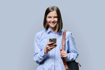 Young woman student with smartphone backpack on grey studio background