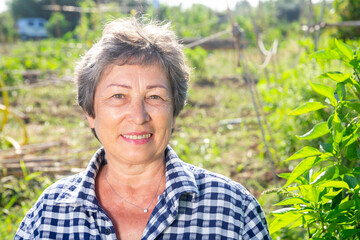 Portrait of retired female amateur gardener posing in homestead with garden equipment