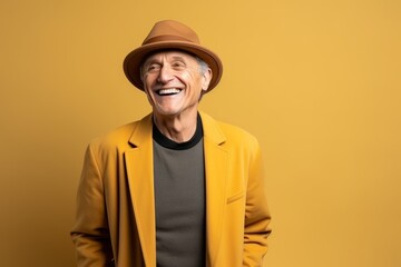 Portrait of smiling senior man in hat and coat on yellow background