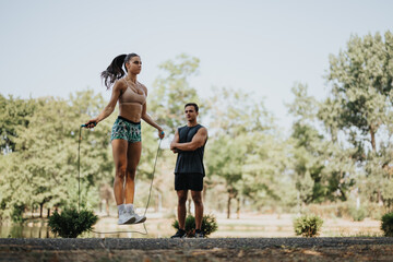 Fototapeta premium Motivated couple jumps rope in park, embracing healthy lifestyle. Fit bodies, persistence, and positive results inspire others. Fresh air fitness and recreation amidst natural environment.