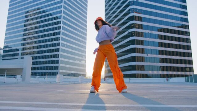 Still camera shot of happy trendy female listening modern music and dancing in summer sunshine. Multi ethnic young girl raising arms enjoying sunset in the city. People energy in downtown slowmo