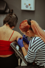 Close up of red haired tattoo artist tattooing a client at the studio