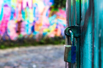 padlock closes a green iron gate with multicolored art concept in blurred graffiti in the background, in Brazil