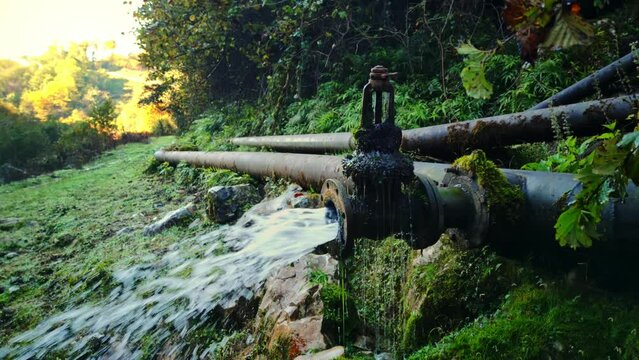Closeup view of pipe in mountain forest with strong stream of water pouring from it filmed in slow motion at summer day. Aqua supply system laid in the rocks and woodland of Georgia. Industrial theme.