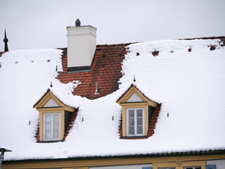 Mit Schnee bedeckte Dachgauben mit Fenstern auf einem barocken Schlossdach