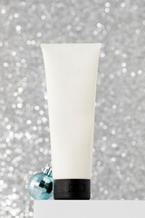 A tube with skin care products with Christmas balls on a bright silver background. New Year's gifts