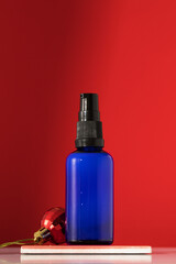 Dispenser with serum or oil for youthful skin on a red background with a Christmas ball. Skin care 