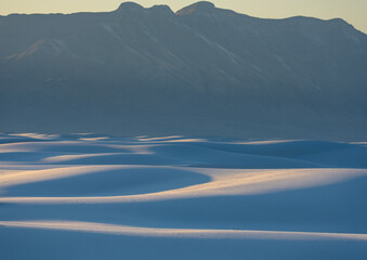 Sand Dunes Sit At The Base of Tall Mountains In White Sands