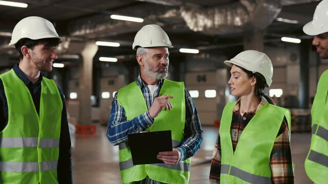 Caucasian Mature Boss Gives Instructions to the Workers Before the Working Day. Diverse Team of Engineering Talking Together. Group of Industry Worker in Factory
