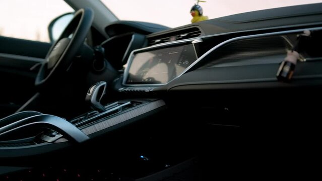 POV video through the open door into the black modern interior of a comfortable car with a screen, multimedia and metal inserts in the evening