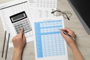 Woman making calculations on calculator at wooden table, top view