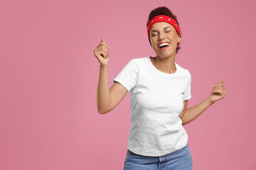 Fototapeta na wymiar Happy young woman in stylish headband dancing on pink background. Space for text