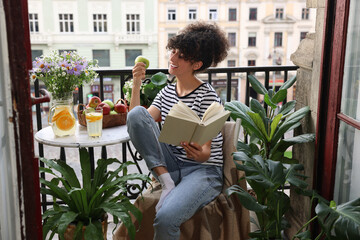 Young woman reading book at table on balcony with beautiful houseplants