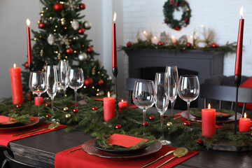 Elegant Christmas table setting with dishware and burning candles in festively decorated room