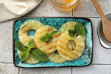 Tasty grilled pineapple slices, honey and wooden spoon on light gray tiled table, flat lay