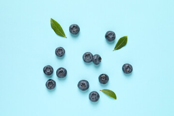 Tasty fresh blueberries with green leaves on light blue background, flat lay