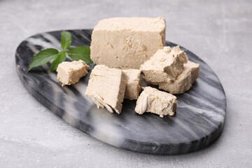 Pieces of tasty halva and mint served on light grey table, closeup