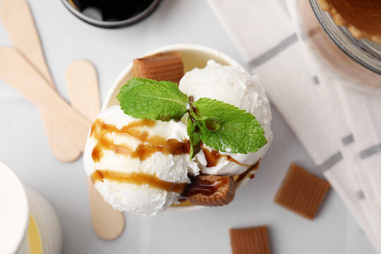 Scoops of tasty ice cream with caramel sauce, mint and candies on white table, top view