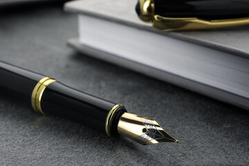 Stylish black fountain pen and notebook on grey textured table, closeup