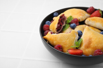 Bowl with delicious samosas, berries and mint leaves on white tiled table, closeup. Space for text