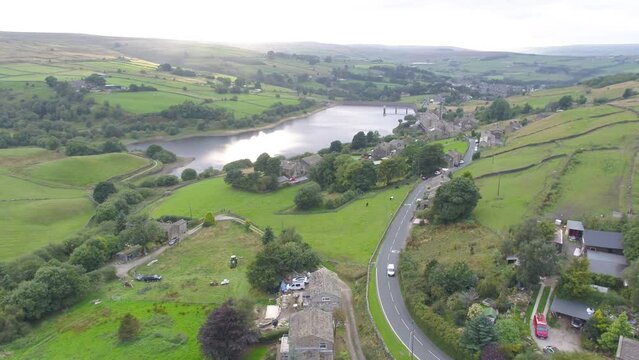 Drone footage panning from the bottom of a small Yorkshire countryside valley to the top of the hill, including village stone houses, farms, country roads, dry stone walls, reservoir and moors