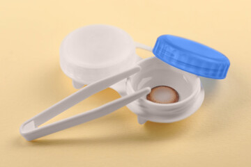 Case with color contact lenses and tweezers on pale yellow background