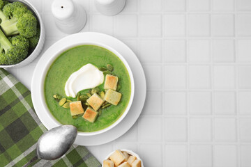 Delicious broccoli cream soup with croutons, sour cream and pumpkin seeds served on white tiled table, flat lay. Space for text