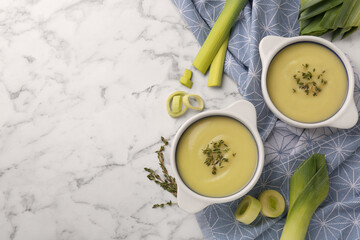Tasty leek soup in bowls on white marble table, flat lay. Space for text