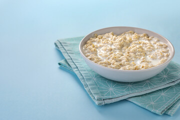 Tasty boiled oatmeal in bowl on light blue table. Space for text