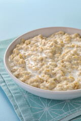 Tasty boiled oatmeal in bowl on light blue table, closeup