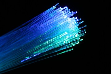 Optical fiber strands transmitting different color lights on black background, macro view