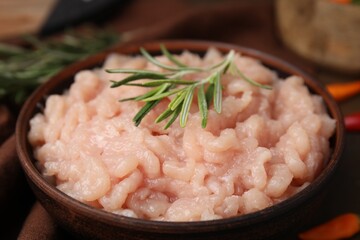 Fresh raw minced meat and rosemary in bowl on table, closeup