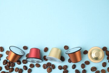 Many coffee capsules and beans on light blue background, flat lay. Space for text