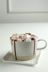 Delicious hot chocolate with marshmallows and cocoa powder in cup on white table