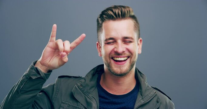 Rock hand gesture, smile or face of man in studio on grey background for freedom, energy or emoji. Happy, male model or portrait of crazy person isolated for devil horns sign, punk or edgy attitude