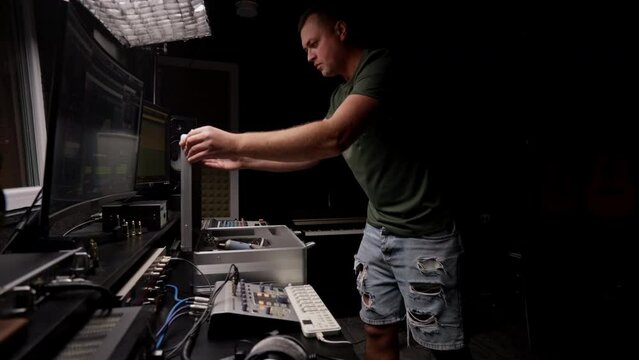 a focused male sound engineer wearing headphones sits at a mixing desk recording new track